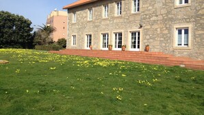 Un edificio in pietra con tetto in tegole rosse, diverse finestre e un prato curato con fiori gialli.