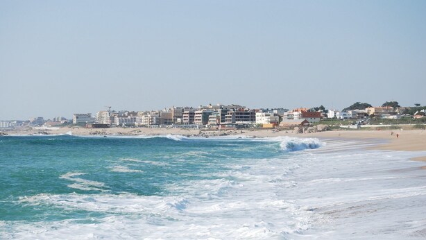 Una spiaggia con onde, edifici sullo sfondo e cielo sereno.