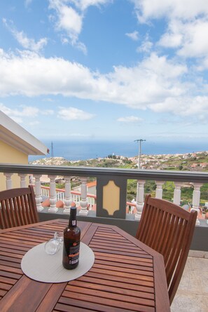 A wooden table with a bottle and glass on a balcony overlooking a coastal town. - Casa Por do Sol, Grab the sun here on our warm terrace. (Ponta do Sol)
