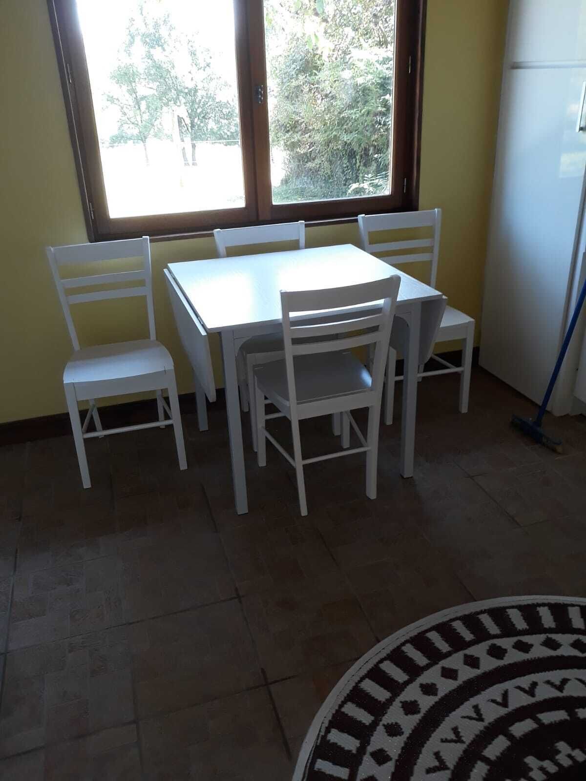 A dining area with a white table and chairs, large windows, and a tiled floor.