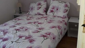 A bedroom with a bed covered in a floral bedspread, two bedside tables with lamps, and a nightstand with a lamp.