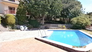 Una piscina con bordo in pietra, circondata da un patio in mattoni. Si vedono gradini che portano a un edificio con un balcone.