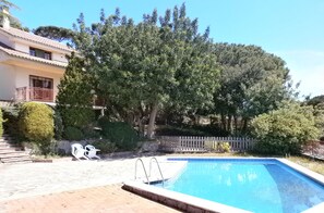 Piscina con borde de piedra, rodeada por un patio de ladrillo. Se observan escalones que conducen a un edificio con balcón.