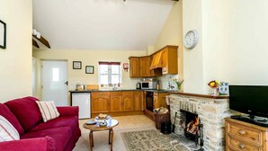 Una sala de estar acogedora con un sofá rojo, una chimenea, un televisor y una cocina al fondo.