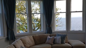 A living room with a beige sectional sofa, a glass coffee table, and a view of the sea through large windows. - Harbour View Apartment with panoramic sea views in Crail (Crail)