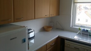A kitchen with wooden cabinets, a white countertop, a toaster, and a window with a view of buildings. - Harbour View Apartment with panoramic sea views in Crail (Crail)