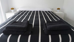 Een bed met zwart-wit strepen, twee witte nachtkastjes met bloevasen, en een witte muur.