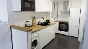 Een moderne keuken met witte kasten, een houten aanrecht, een ingebouwde wasmachine, een zwarte magnetron, een roestvrijstalen afzuigkap en een witte koelkast.