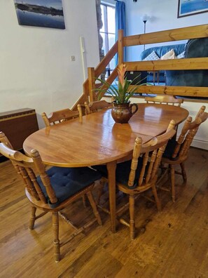 Una mesa de madera para comer con seis sillas, una planta en maceta y una escalera al fondo.