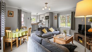 A living room with a grey sofa, wooden coffee table, and a TV stand. There is a dining area with a table and chairs. - Two bedroom lodge within walking distance of Lynton Centre. Free fishing onsite (Lynton)