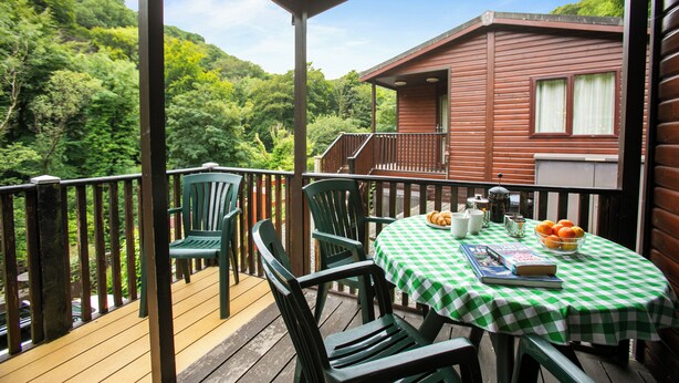 A wooden deck with a table and chairs, a book, and a bowl of fruit. - Two bedroom lodge within walking distance of Lynton Centre. Free fishing onsite (Lynton)