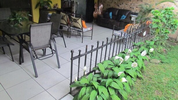 An outdoor patio with a tiled floor, a black leather sofa, and a dining table with chairs.