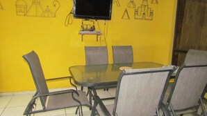 A conference room with a glass table, four chairs, a television on a stand, and a yellow wall with architectural drawings.