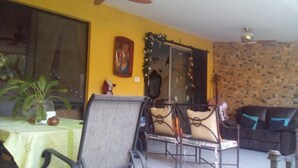 A room with a yellow wall, a large window, a dining table with chairs, a sofa, and a decorative mirror.