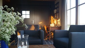 A cozy room with two dark blue armchairs, a wooden coffee table, a glass vase with white flowers, and a small table with a lamp and a cross on the wall. - Holiday home 't Ligt ter velde (Lichtervelde)