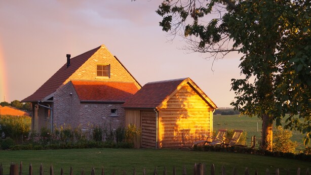 A rustic barn with a brick extension and a wooden shed, surrounded by a fenced yard and a tree. - Holiday home 't Ligt ter velde (Lichtervelde)