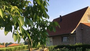 A brick house with a red roof, surrounded by a well-maintained garden with various plants and a wooden gate. - Holiday home 't Ligt ter velde (Lichtervelde)