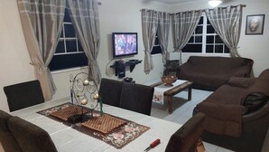 Un salon comprenant une télévision, un canapé, une table à manger et des rideaux.