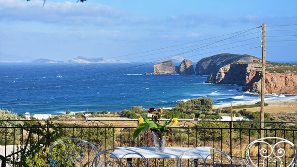 A balcony with a view of the ocean and cliffs, a vase with flowers, and a metal railing. - Villa with Amazing Sea View (Naxos)
