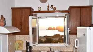 A kitchen with wooden cabinets, a window with a view of the sea, a sink, and a coffee maker. - Villa with Amazing Sea View (Naxos)