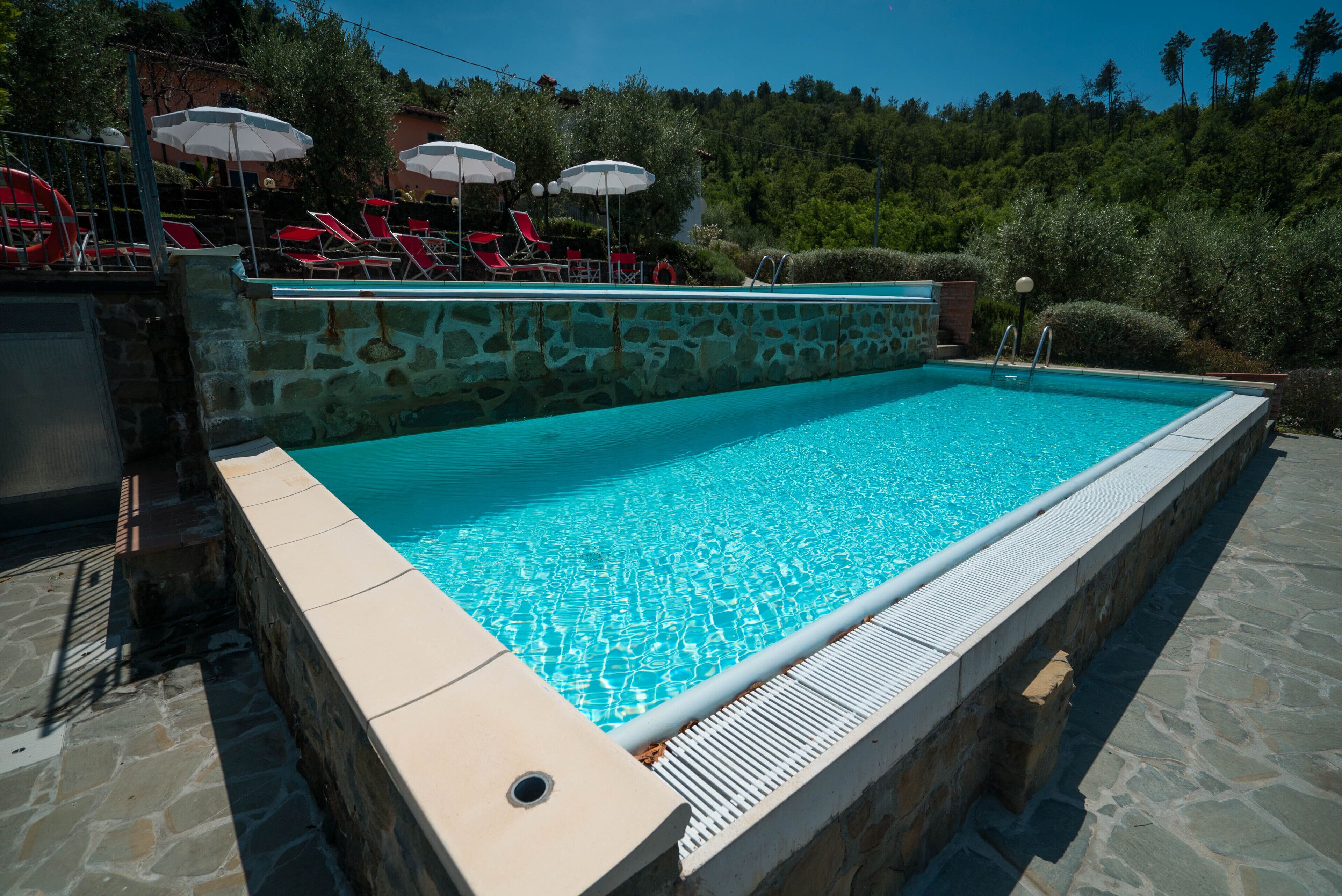 A rectangular swimming pool with a stone wall and a tiled deck.