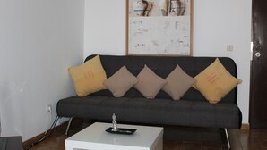 Un salon moderne avec un canapé gris foncé, quatre coussins et une table basse blanche agrémentée d’un objet décoratif.
