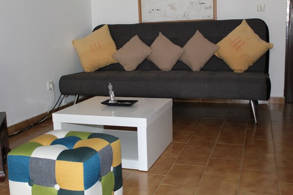 A living room with a sofa, a white coffee table, and a colorful ottoman.
