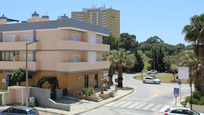 Un immeuble résidentiel à plusieurs étages doté de balcons, une rue bordée de voitures et des palmiers.