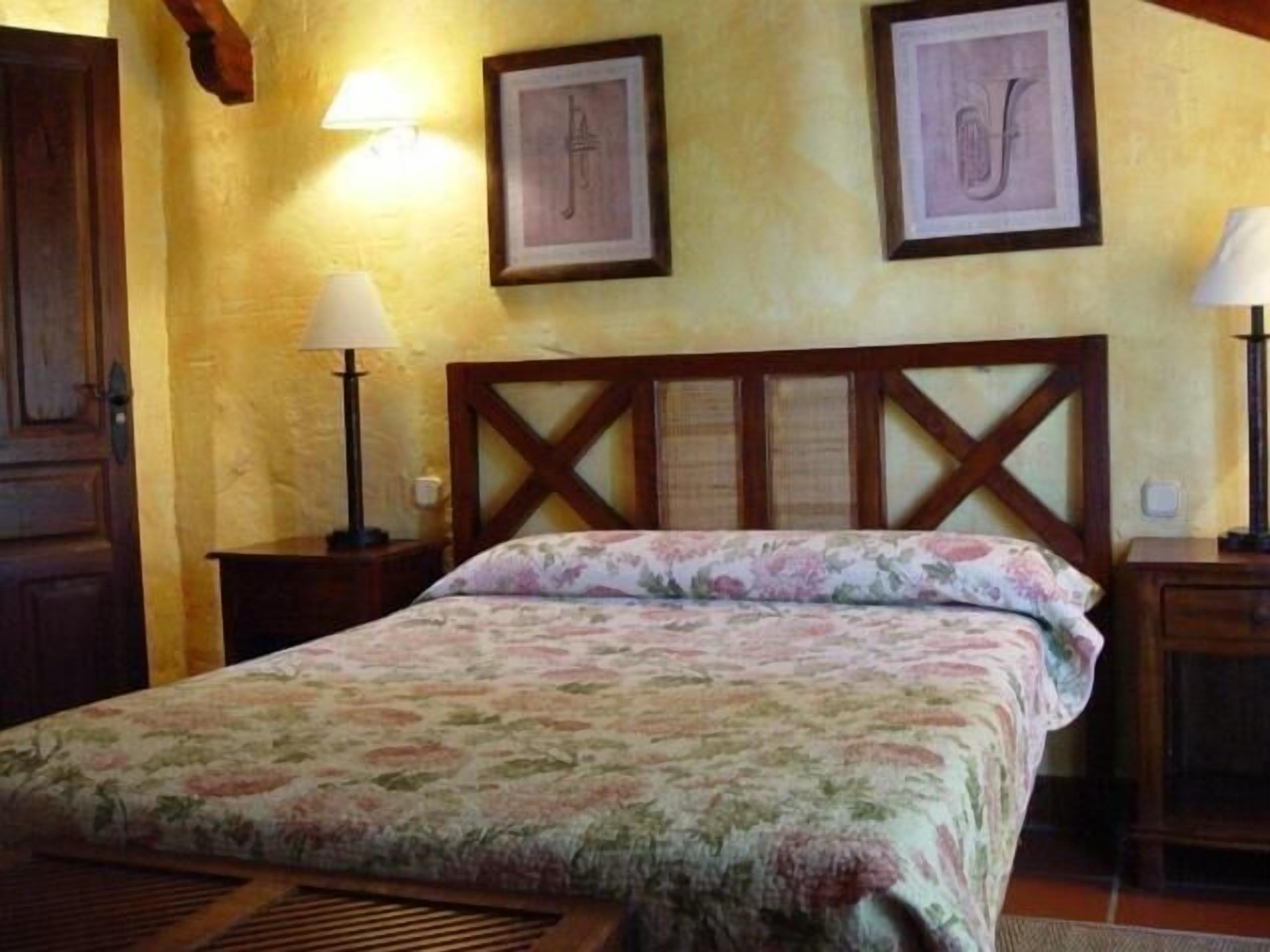 A bedroom with a wooden headboard, floral bedding, two bedside lamps, and framed artwork on the wall.