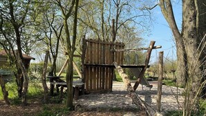 Un portón de madera rústico con un columpio, rodeado de árboles y rocas.