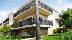 A multi-story building with balconies, a garage, and lush greenery. - Exclusive Luxury Apartment, Garden Backing On First Green (Lagos)