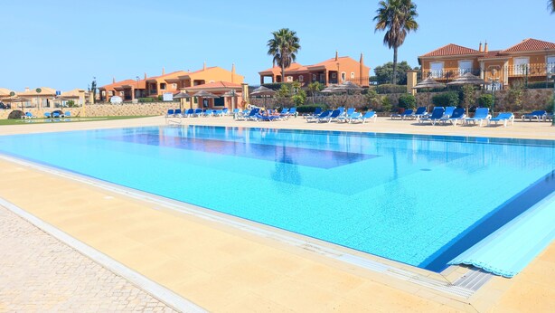 A large swimming pool with blue water, surrounded by lounge chairs and umbrellas. - Exclusive Luxury Apartment, Garden Backing On First Green (Lagos)