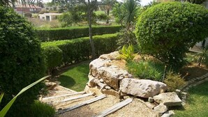 A landscaped garden with a rock formation, gravel path, and various shrubs. - Exclusive Luxury Apartment, Garden Backing On First Green (Lagos)