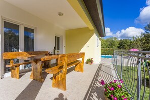 A wooden bench and table set on a balcony with a view of a swimming pool and greenery. - Holiday home for 6, 90 m² with private pool 40m² (Zminj)