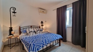 A bedroom with a bed, two bedside tables, a wall-mounted air conditioner, a window with curtains, and a decorative wall hanging. - Holiday home for 6, 90 m² with private pool 40m² (Zminj)