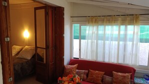 A room with a red sofa, a wooden door, and a window with sheer curtains.