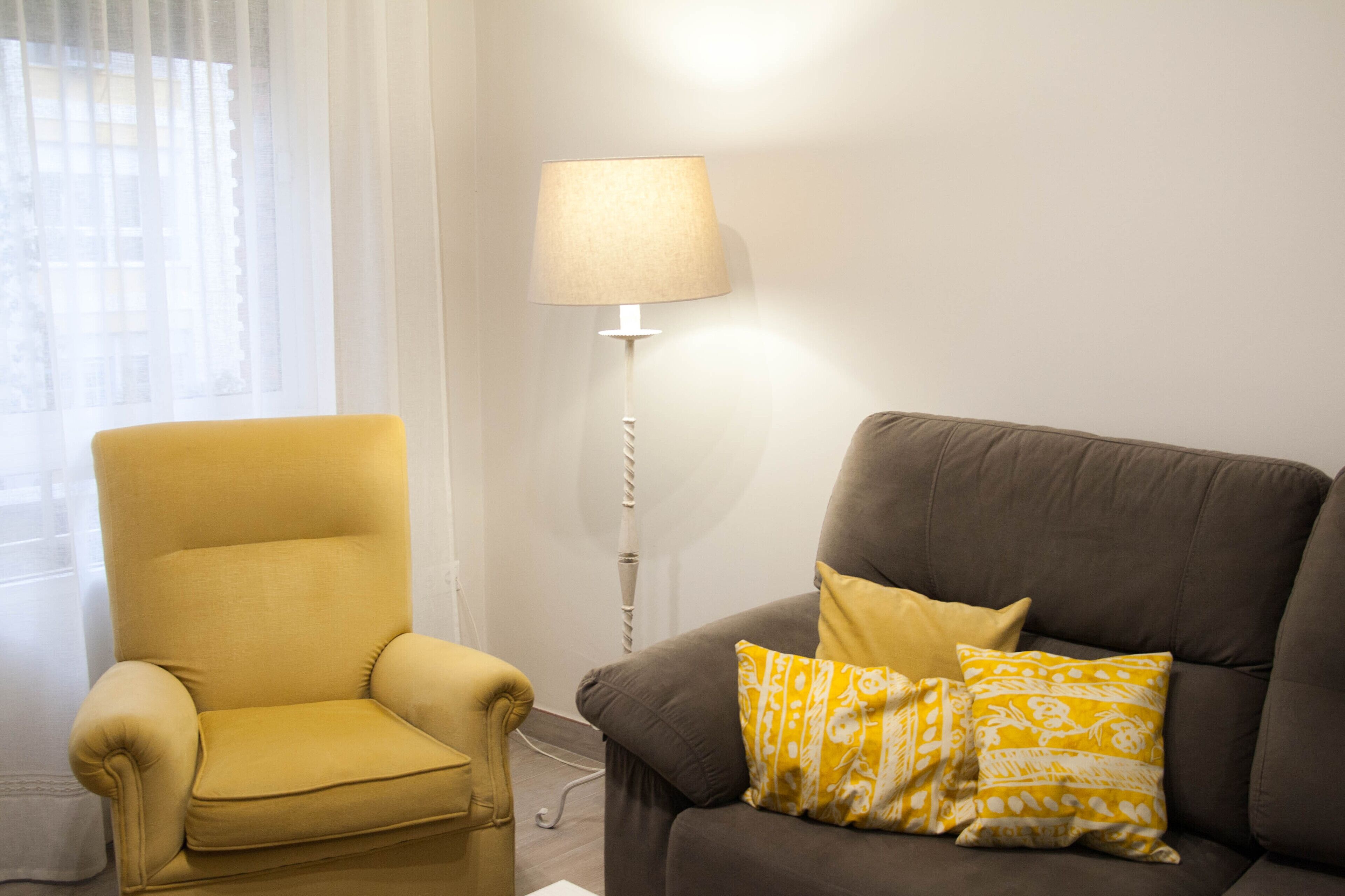 Un soggiorno con una poltrona gialla e un divano marrone con cuscini decorati.