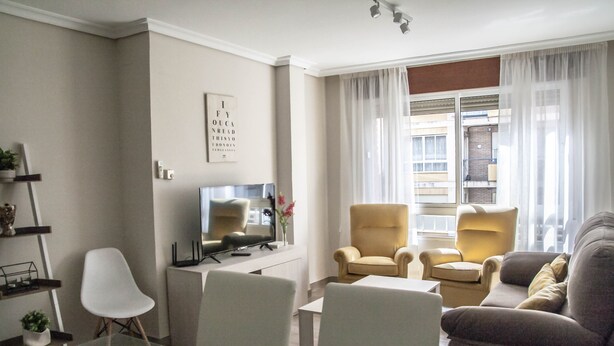 Un salon moderne avec un téléviseur à écran plat, deux fauteuils, un canapé et une table basse en verre.
