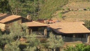 Una casa rural con techo de tejas, rodeada de vegetación y colinas.