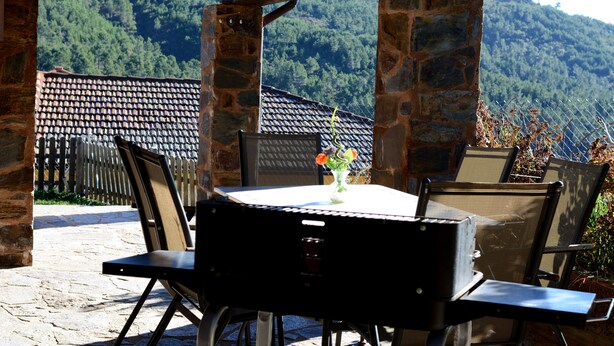 Un patio al aire libre con pilares de piedra, una mesa con sillas y vistas a una montaña boscosa.