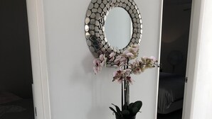 Une coiffeuse blanche avec un miroir rond et une orchidée en pot.
