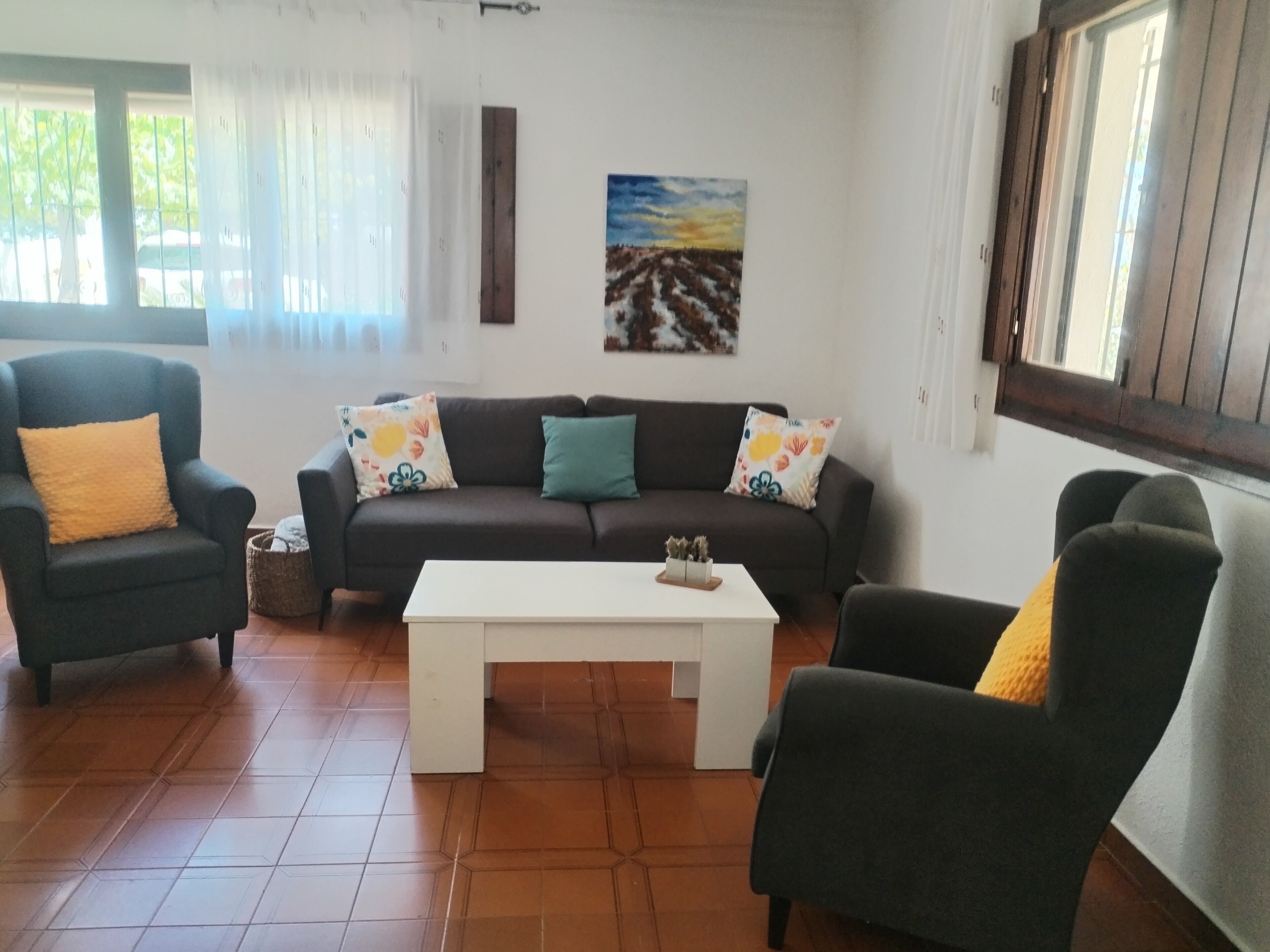 Un salon comprenant un canapé, deux fauteuils, une table basse et un tableau accroché au mur.
