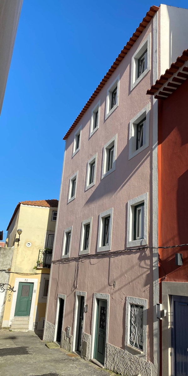A multi-story building with a red-tiled roof, multiple windows, and a green door. - Sta Clara House- Central & Quiet. Bright Studio (Lisboa)