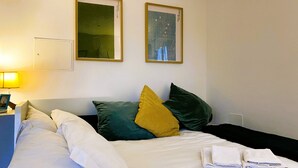 Habitación de hotel con cama, almohadas, mesita de noche, lámpara y dos cuadros en la pared.