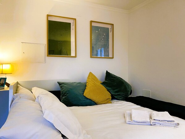 Een hotelkamer met een bed, kussens, een nachtkastje, een lamp en twee ingelijste kunstwerken aan de muur.