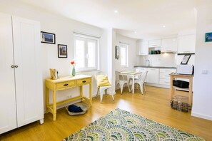 Een ruimtelijk ingerichte leefruimte met kitchenette, eethoek en een klein werkplekje.
