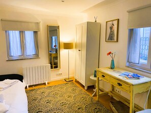 Une chambre d’hôtel comprenant un lit, un bureau, une armoire, un radiateur, un miroir et une fenêtre avec des rideaux.