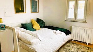 A bedroom with a bed, pillows, a bedside table, a lamp, a radiator, and two framed pictures on the wall.