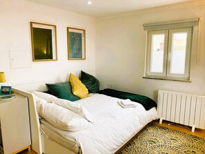 Un dormitorio con cama, almohadas, una mesita de noche, lámpara, radiador y dos cuadros en la pared.