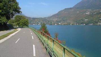 Una carretera con barandilla verde, un lago y una montaña al fondo.